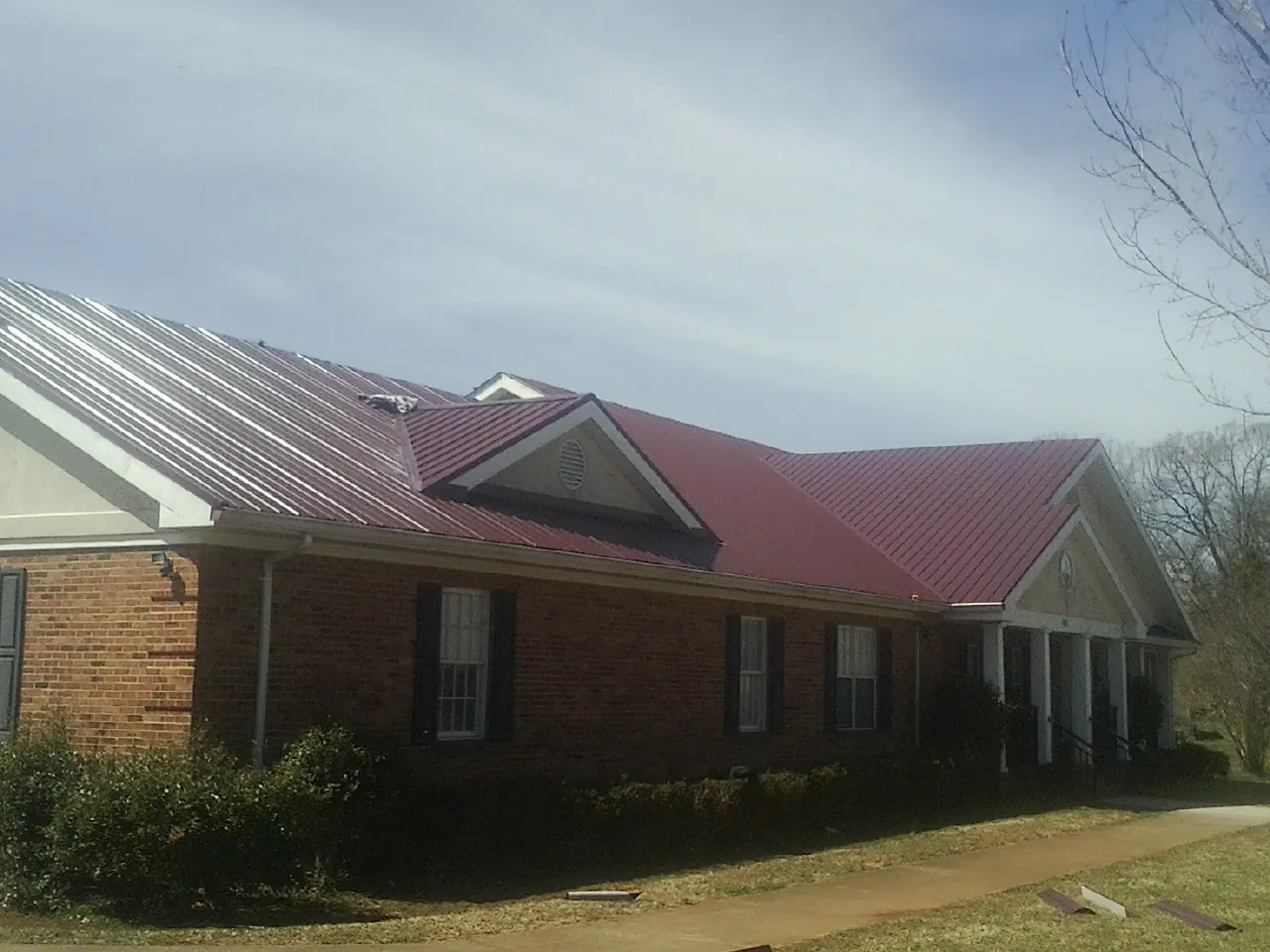 Red metal roof with gabled entries on a long brick building, from a Hail Damage Roof Repair job in Loreauville