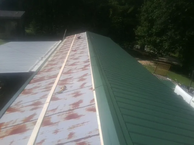 Old rusted panels beside newly installed green metal roofing — Wind Damage Roof Repair by Roofing Brothers in Loreauville