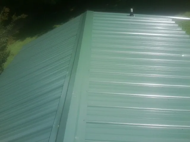 New green metal panels meeting at the ridge of a roof — Flat Roof Repair work by our crew in Loreauville