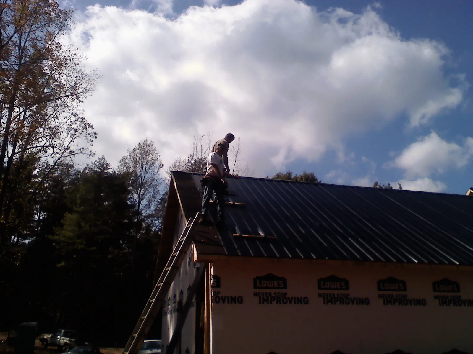 Roofer fastening dark metal panels high against a cloudy sky, from a Roof Inspection job in Loreauville