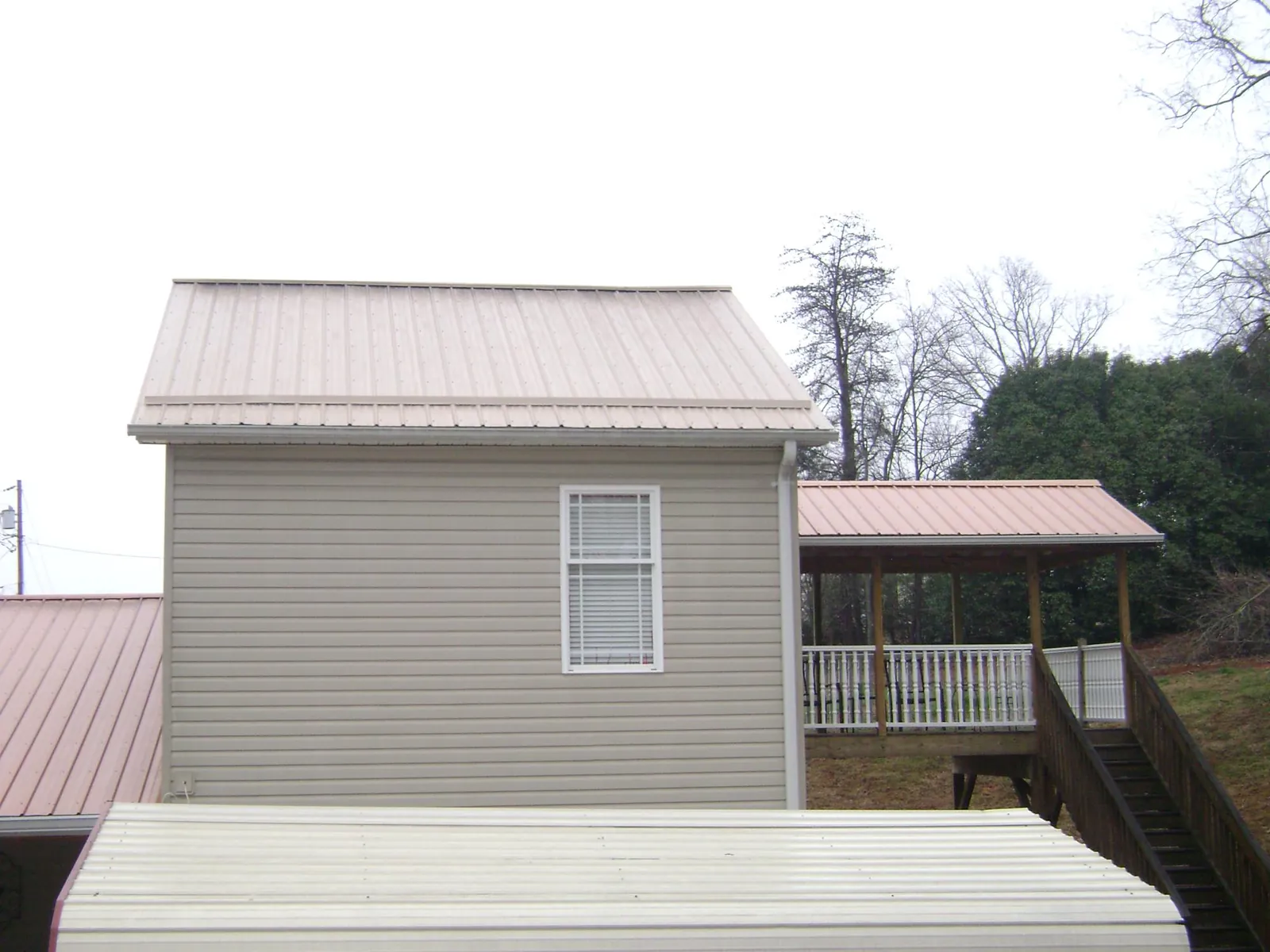 Tan metal roofs on a two story addition and attached porch, from a Roof Replacement job in Loreauville